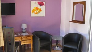 A room with a desk, two black chairs, a small round table, a TV mounted on the wall, and a painting of flowers.