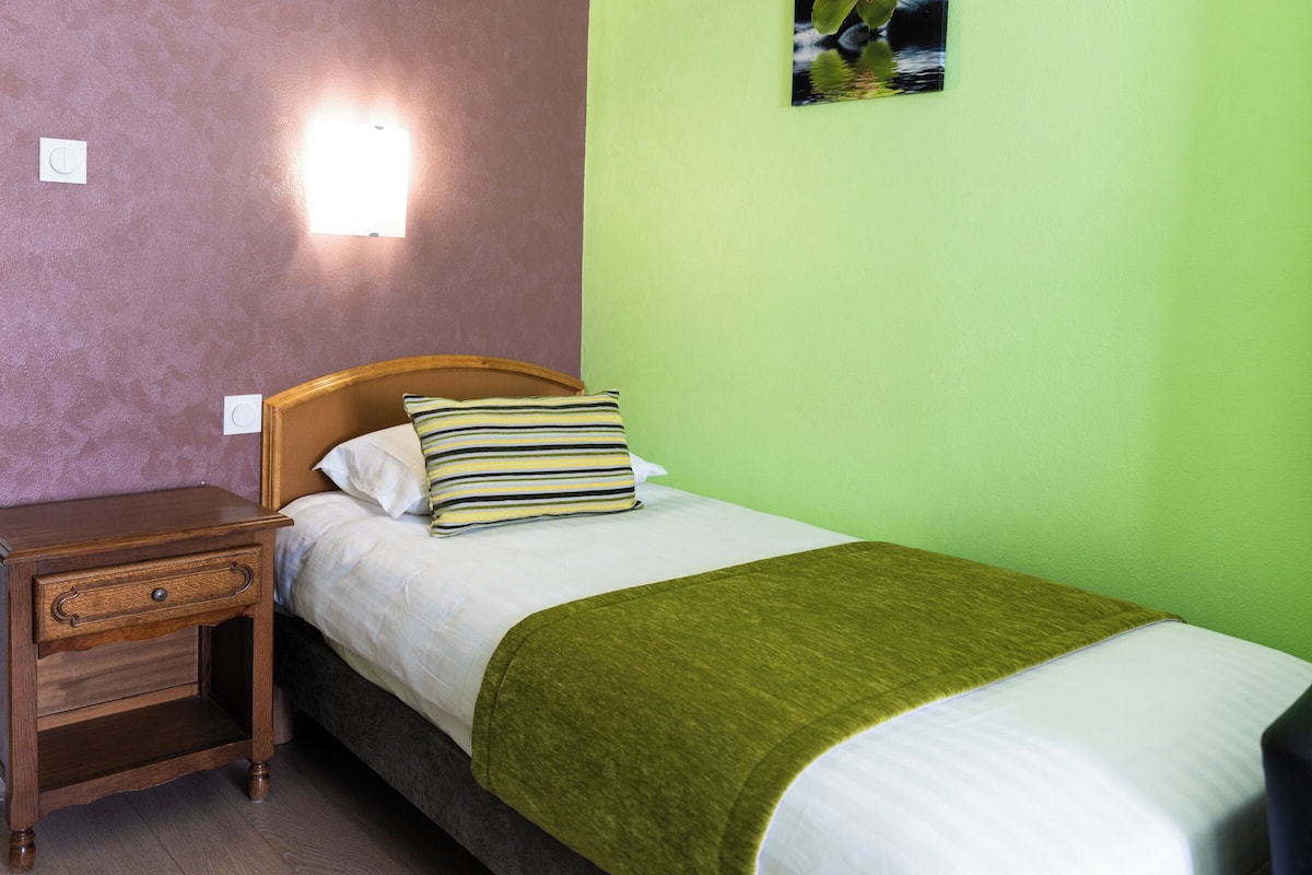 A neatly made bed with a striped pillow, a wooden nightstand with a drawer, and a green wall.