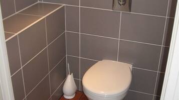 A small bathroom with a toilet, a bidet, and a wall-mounted flush handle.