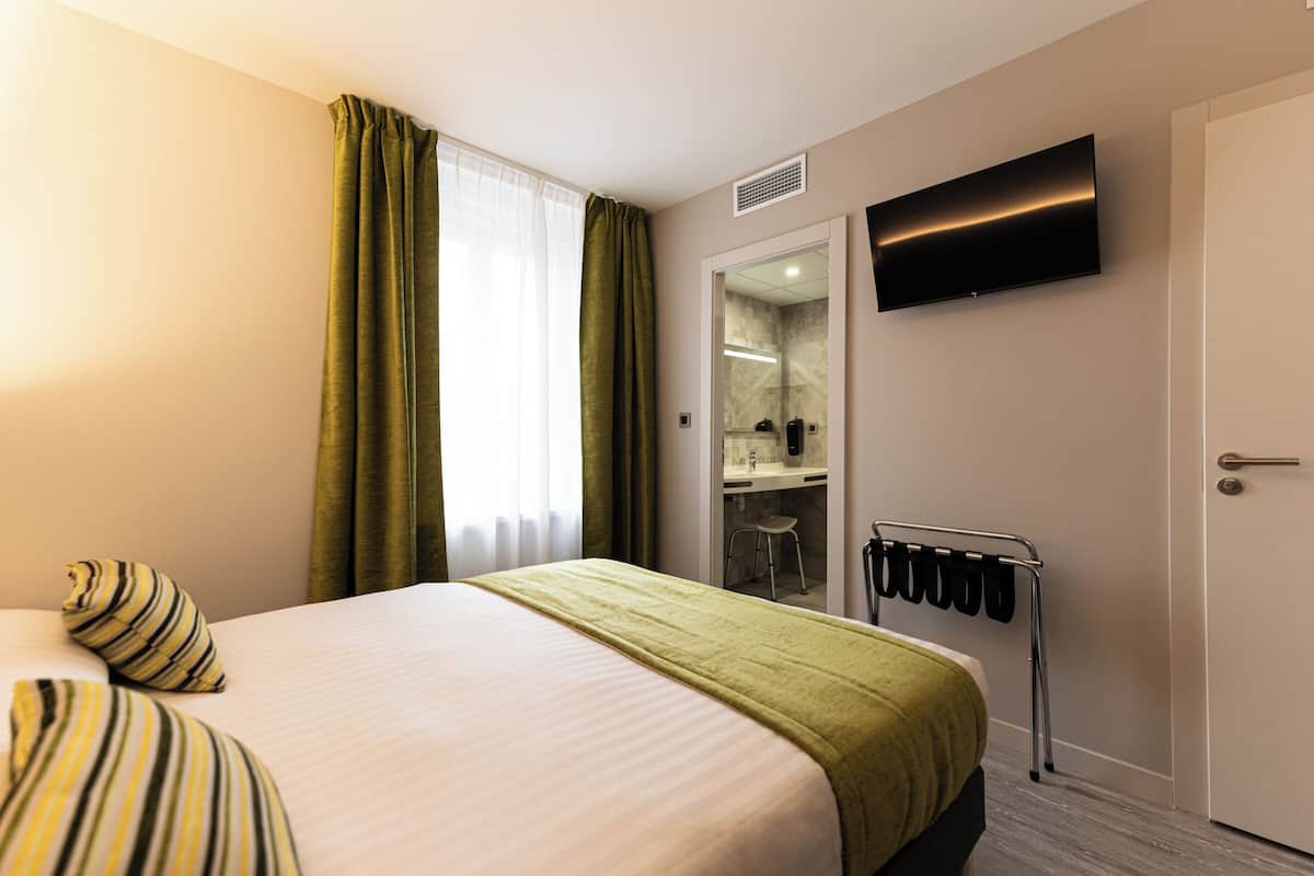 A hotel room with a bed, a television mounted on the wall, a mirror, and a coat rack.