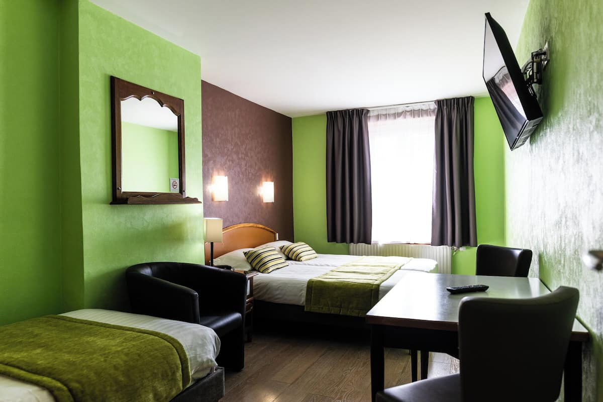 A hotel room with a bed, two chairs, a table, a TV, and a window with curtains.