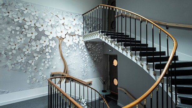 A modern staircase with a wooden handrail and black steps, leading to a landing with a decorative wall and a skylight above.