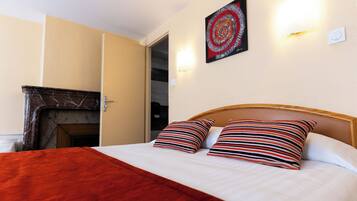 Quarto de hotel com cama, almofadas listradas, manta vermelha, lareira e uma obra de arte na parede.