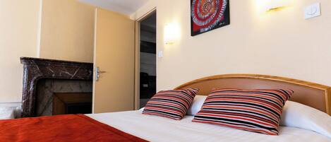 Una habitación de hotel con cama, almohadas a rayas, una manta roja, una chimenea y una obra de arte en la pared.