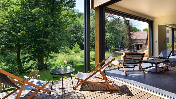 An outdoor deck with wooden furniture, a glass table, and a view of a forested area. - Moulin des Templiers Hôtel & SPA (Pontaubert)