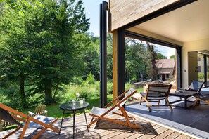 An outdoor deck with wooden furniture, a glass table, and a view of a forested area. - Moulin des Templiers H ôtel & SPA (Pontaubert)