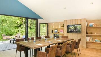 A modern meeting room with a large wooden table and chairs, a television, and bookshelves.