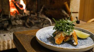 A plate of food with a slice of lime on a patterned plate, set on a wooden table with a fireplace in the background.