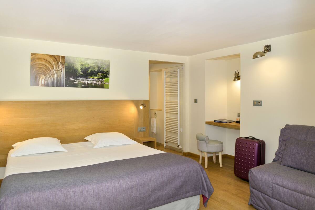 Une chambre d’hôtel avec un lit, un bureau, une chaise et une valise.