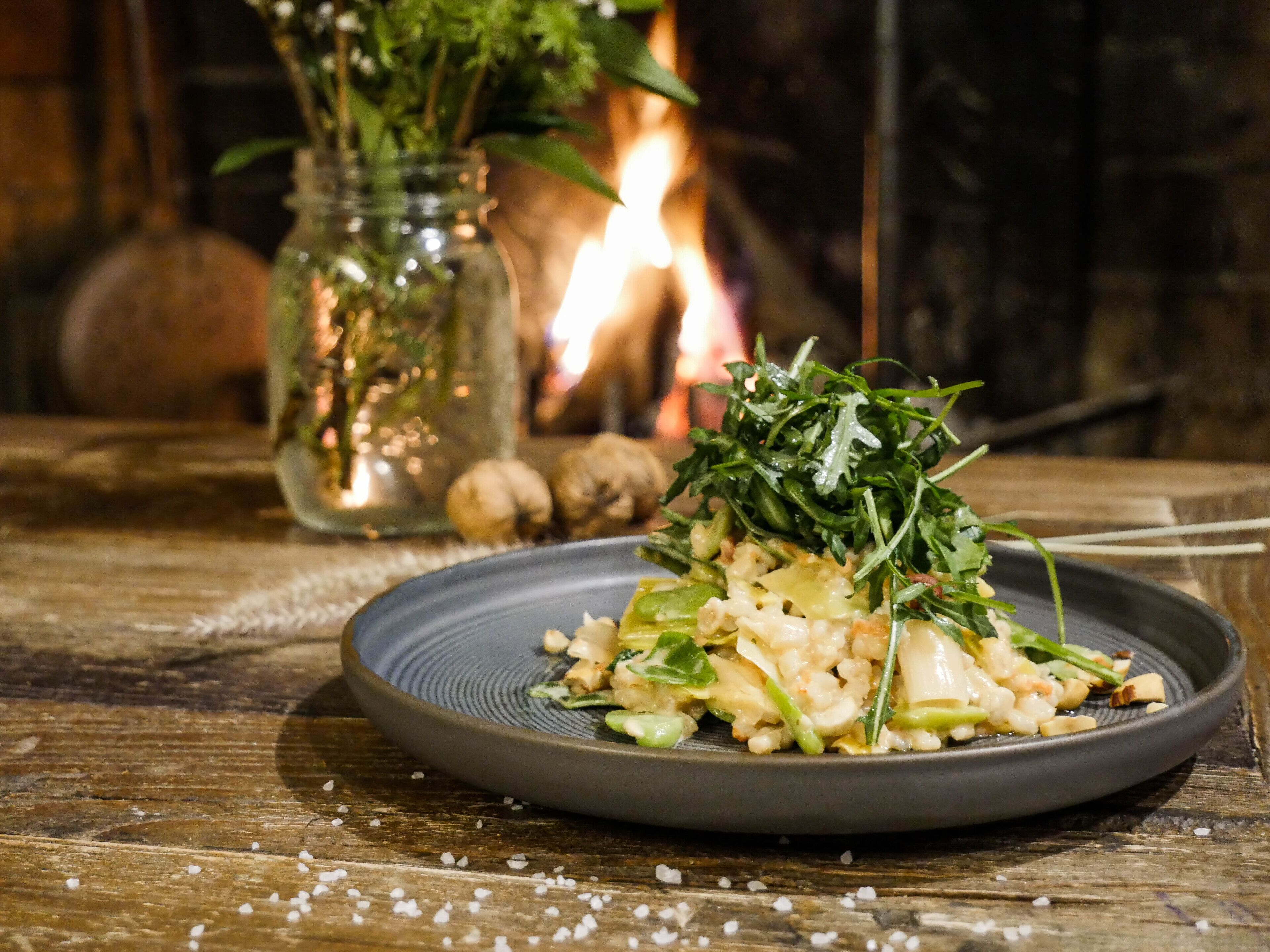 A plate of food on a wooden table with a rustic setting, including a candle and a jar of herbs in the background.