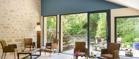 A spacious living area with a large window overlooking a garden, furnished with modern chairs and a wooden coffee table.