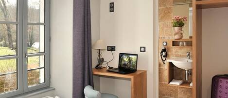 A hotel room with a desk, chair, laptop, radiator, and a view of the outdoors.