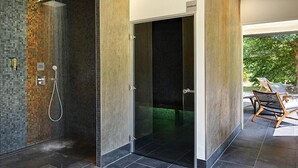 A modern bathroom with a glass shower enclosure, a visible toilet, and a door leading to an outdoor area with chairs. - Moulin des Templiers Hôtel & SPA (Pontaubert)