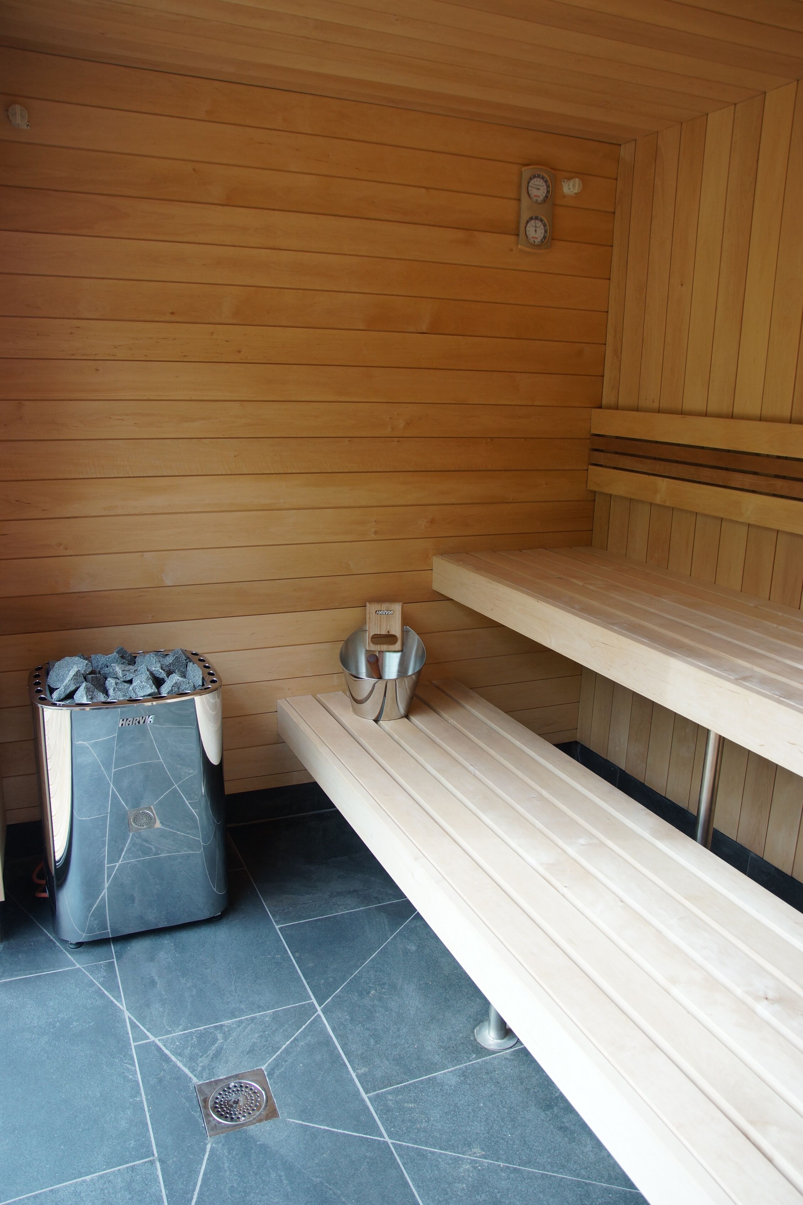 A sauna with wooden walls, a bench, a stone heater, and a metal bucket.
