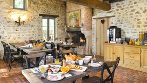 A rustic dining area with stone walls, a brick fireplace, wooden furniture, and a variety of breakfast items on the table. - Moulin des Templiers Hôtel & SPA (Pontaubert)