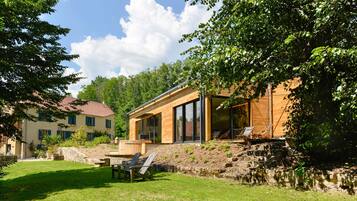 Ein modernes Haus mit großem Glasfenster, einer Holzdielen-Terrasse und einer Steinmauer.