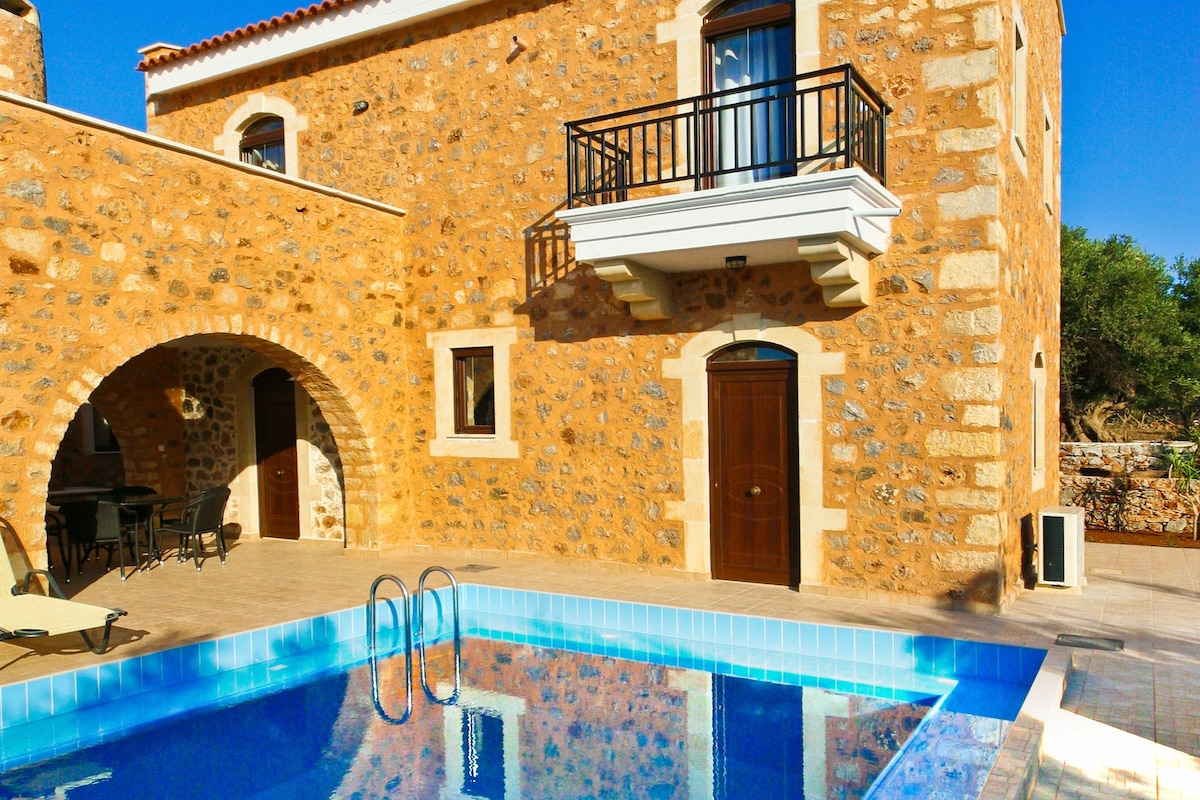 A stone building with a swimming pool, a balcony, and an arched doorway.