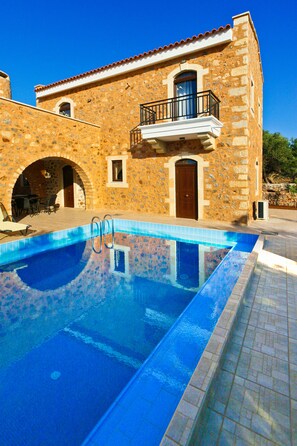 A stone building with a swimming pool, a balcony, and an arched doorway.