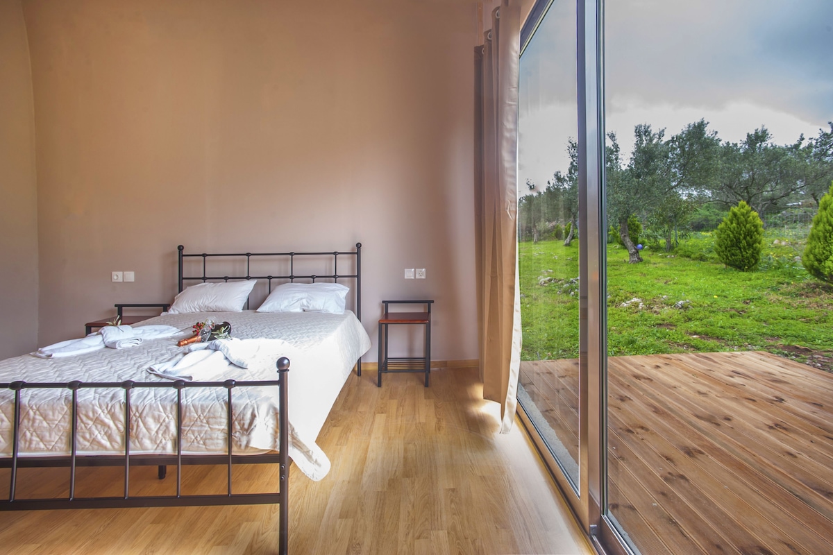 A bedroom with a bed, bedside tables, and a large window overlooking a garden.