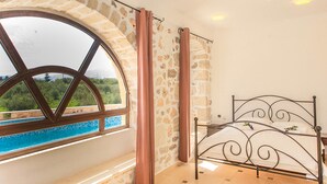 A room with a stone wall, a large arched window, and a metal bed frame. - Villas and Bungalows (Apokoronas)