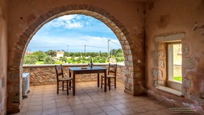 An outdoor patio with a stone table and chairs, a view of the countryside, and a stone archway. - Villas and Bungalows (Apokoronas)