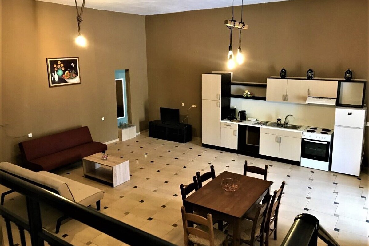 A compact living space with a sofa, dining table, chairs, a kitchen area with cabinets and appliances, and a staircase.