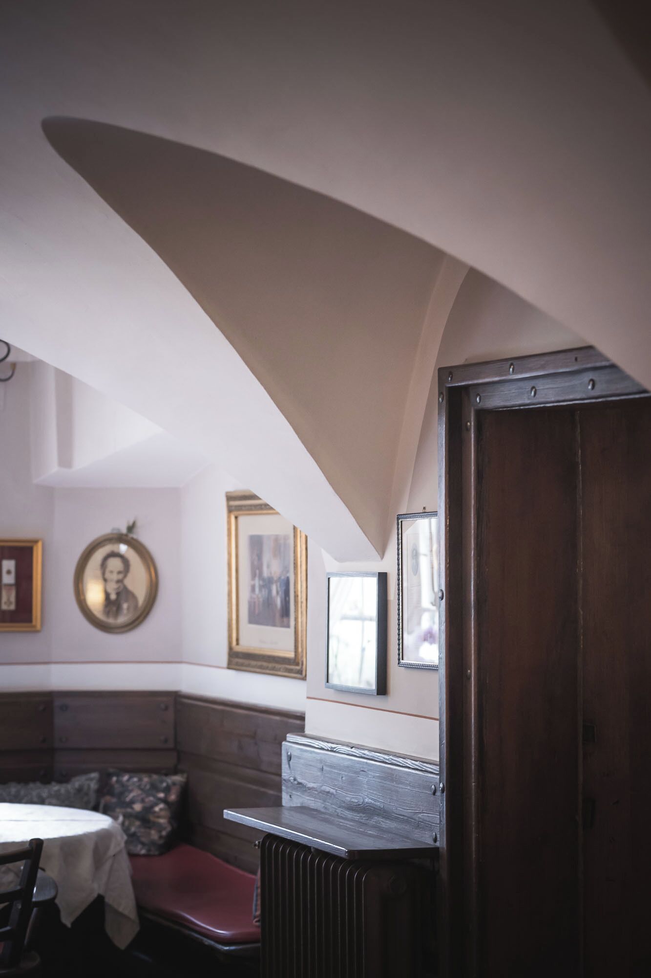 Une pièce avec un plafond en pente, un banc, une table et des tableaux encadrés accrochés au mur.