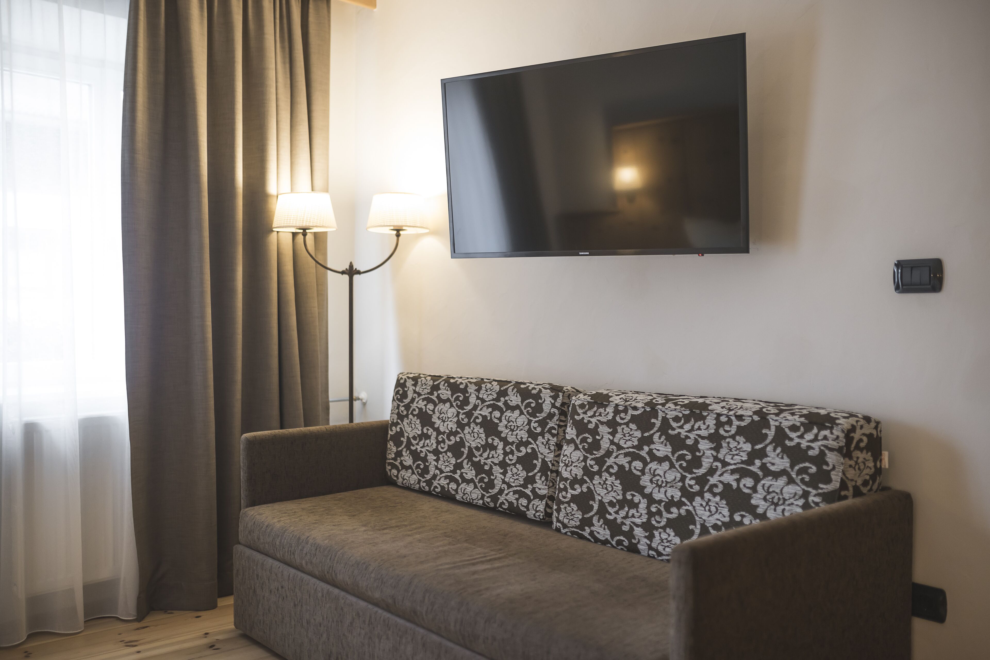 A modern living room with a sofa, a flat-screen TV mounted on the wall, and a floor lamp.