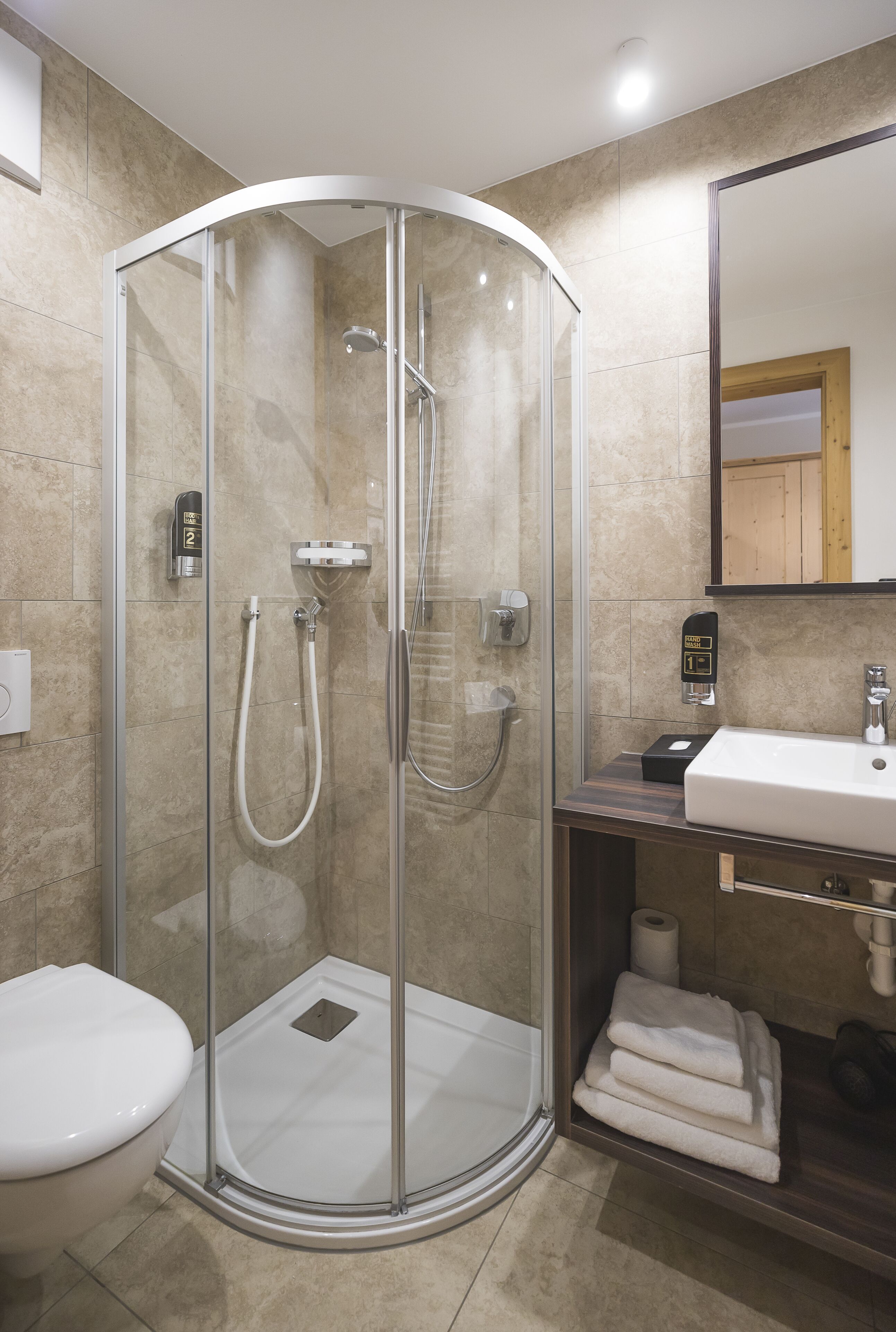 Ein modernes Badezimmer mit einer begehbaren Glasdusche, einem weißen Waschbecken und einem Spiegel darüber.