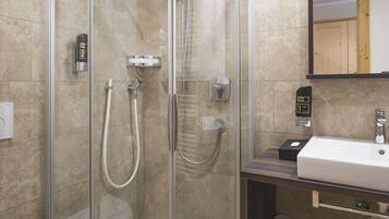 Ein modernes Badezimmer mit einer begehbaren Glasdusche, einem weißen Waschbecken und einem Spiegel darüber.