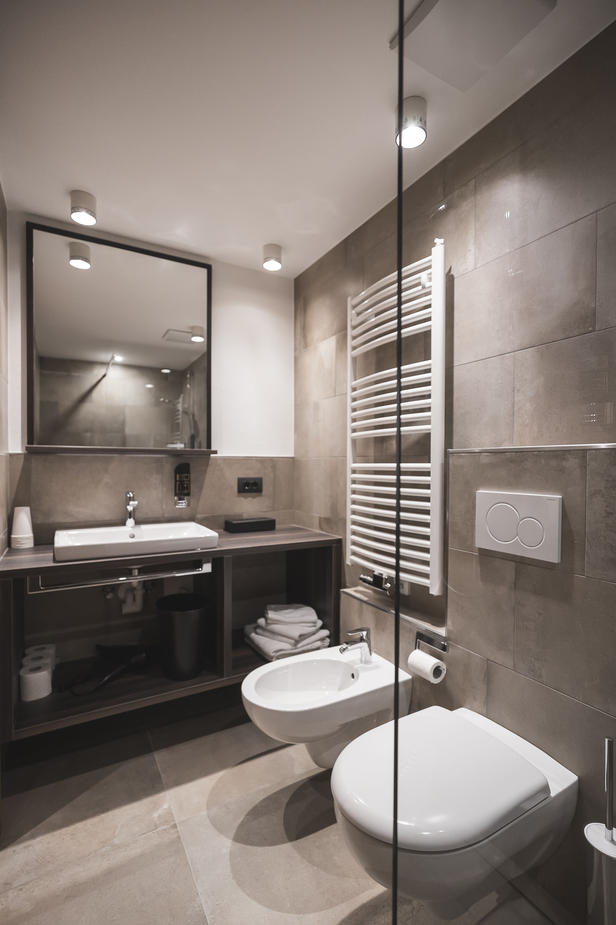 A modern bathroom with a sink, mirror, toilet, and towel warmer.