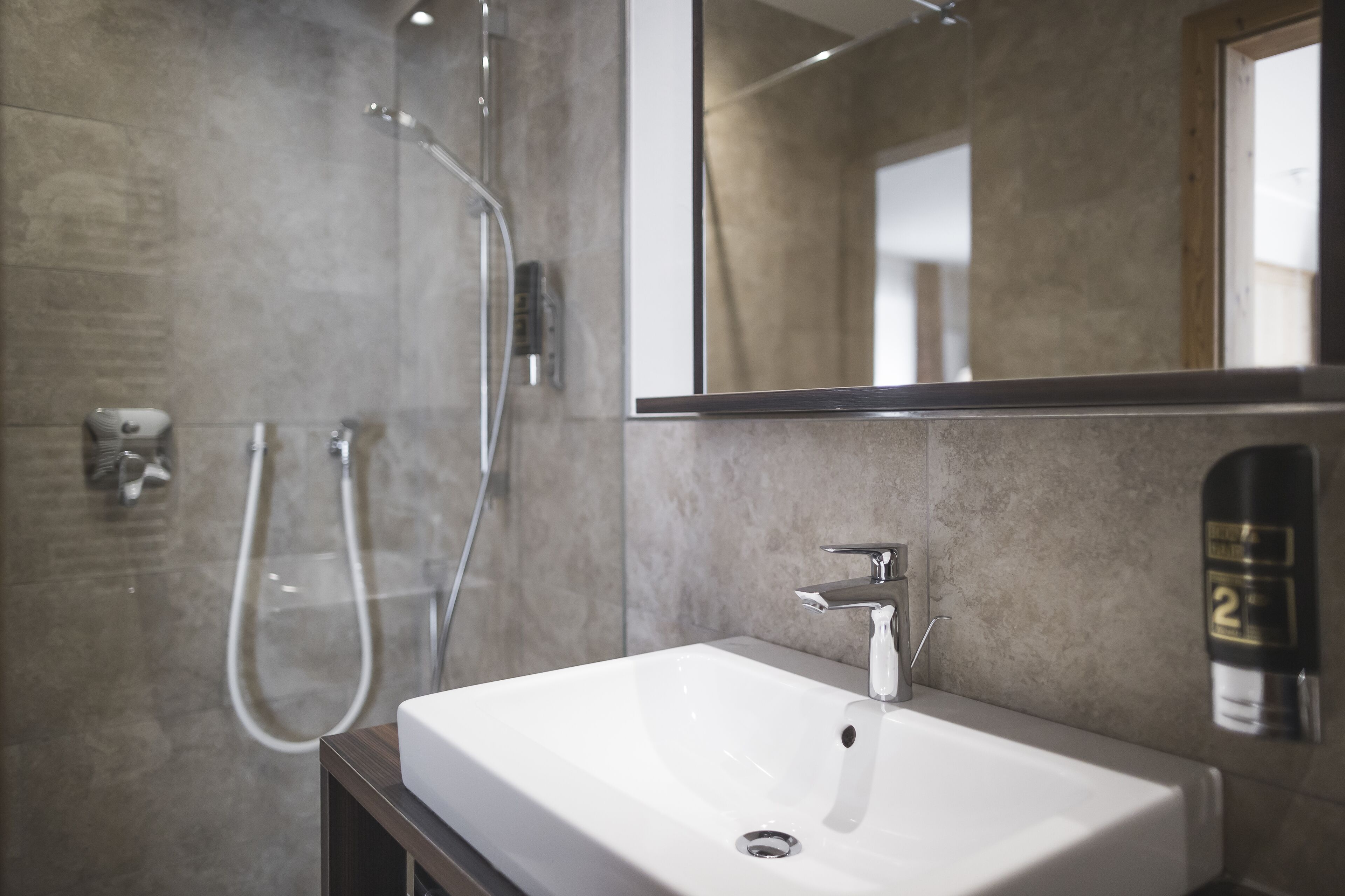 Een moderne badkamer met een witte wastafel, een handdouche en een grote spiegel.