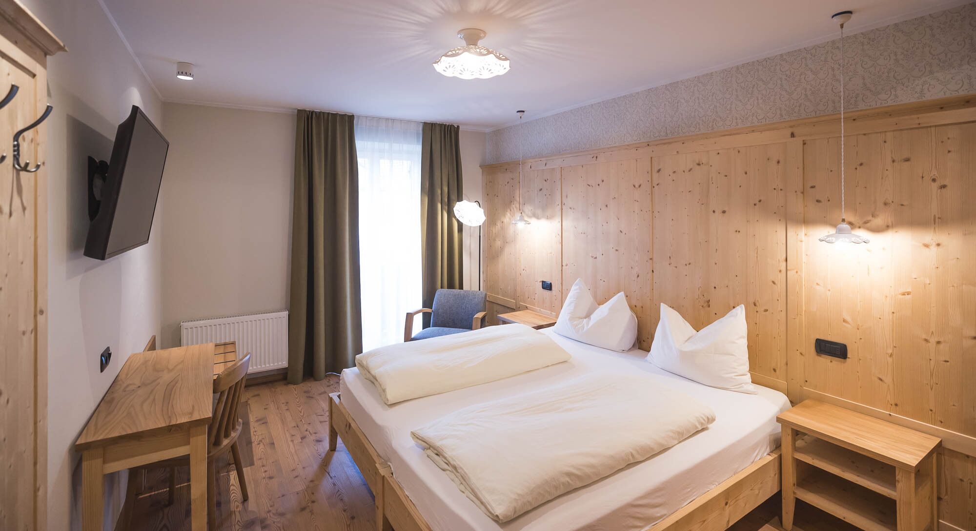 Una habitación de hotel con una cama grande, un escritorio, una silla y un televisor en la pared.