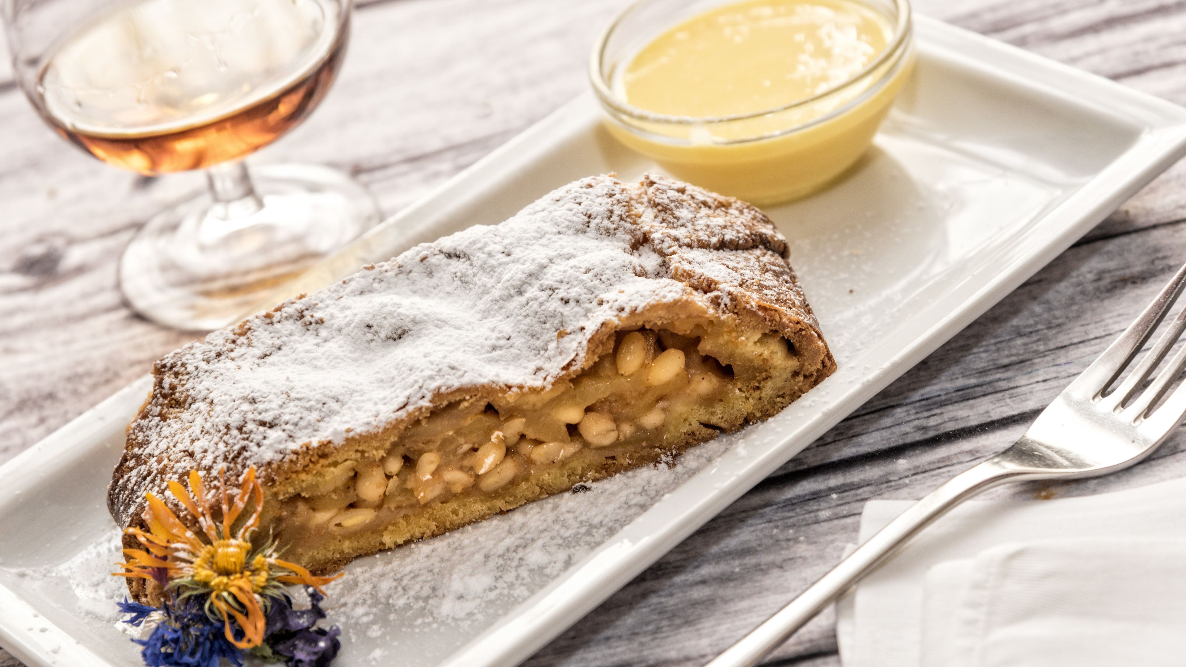 A dessert with powdered sugar, a glass of a beverage, and a fork on a tray.