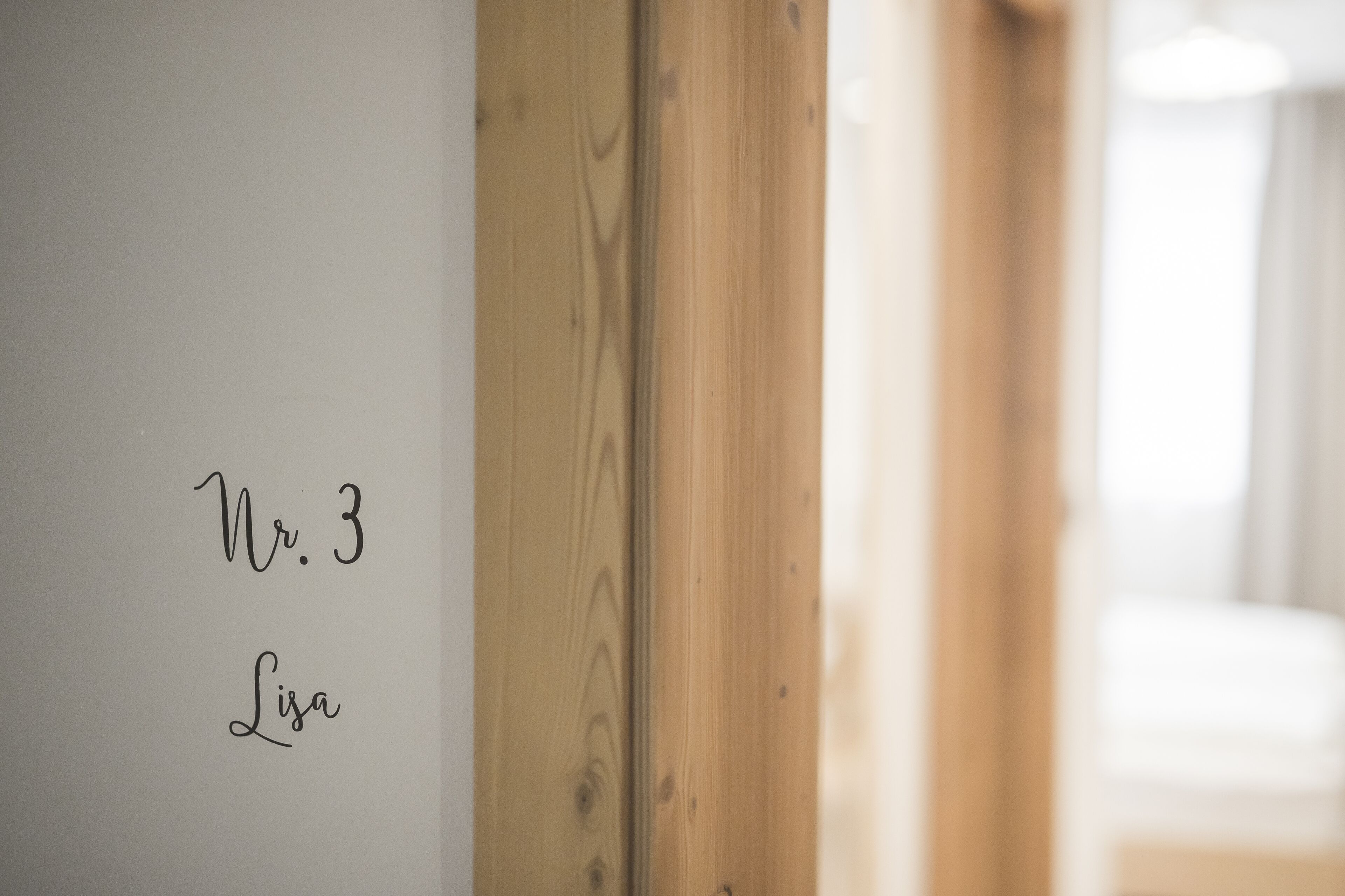 A wooden door with a white wall beside it, displaying the text "Nr. 3 Lisa".