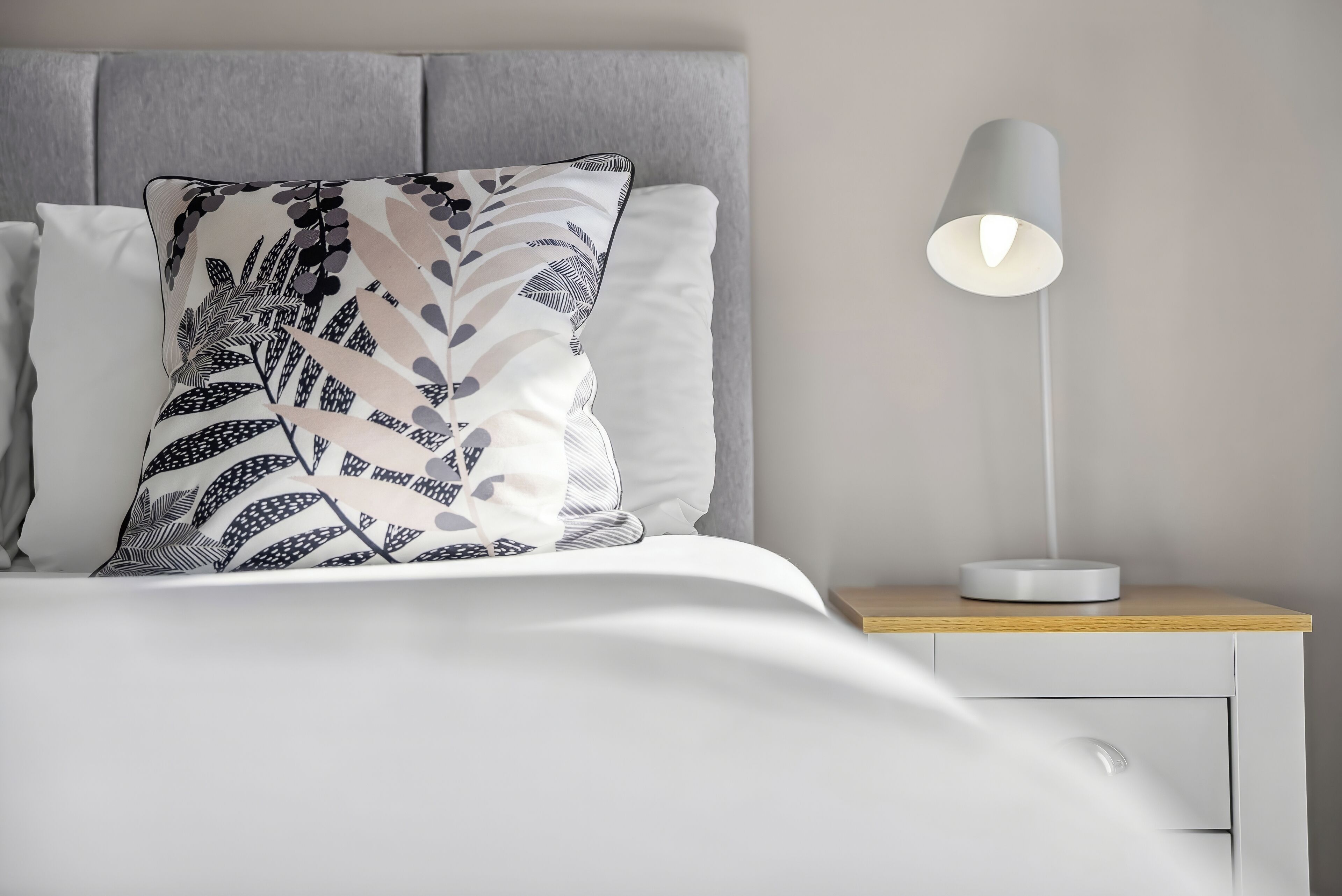 A neatly made bed with a patterned pillow, a bedside lamp, and a wooden nightstand.