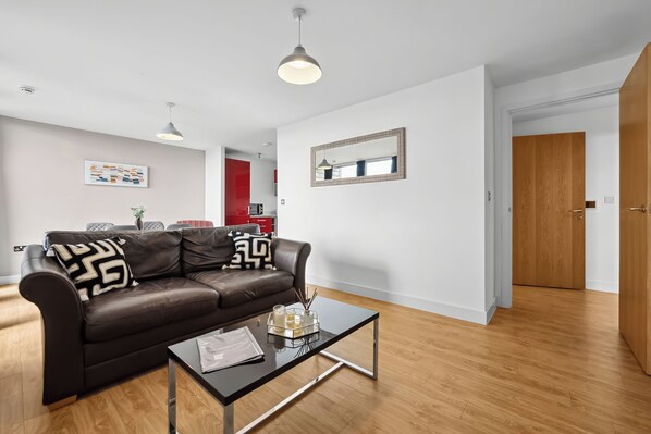 A modern living room with a brown leather sofa, a glass coffee table, and a wooden floor. - Cotels at Vizion (Milton Keynes)
