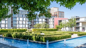 Un espace piscine moderne, agrémenté d’un aménagement paysager aux formes géométriques et bordé de bâtiments contemporains.