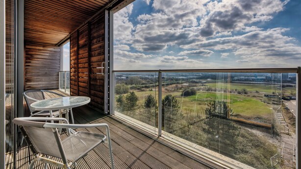 Un balcon doté d’une table et de chaises, offrant une vue sur un paysage rural avec des champs et des arbres.