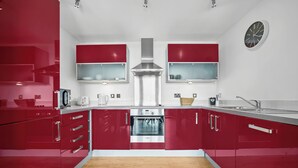 Une cuisine moderne avec des meubles de rangement rouges, un four en acier inoxydable et un plancher en bois.