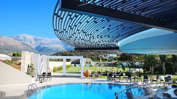 A pool area with a modern architectural canopy, lounge chairs, and a view of mountains.
