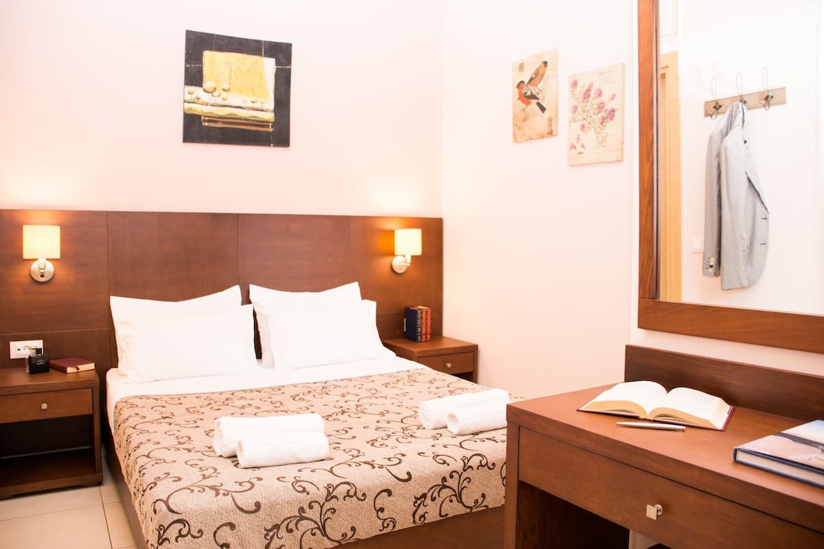 Una camera d'albergo con un letto, abat-jour, comodini, una cassettiera e uno specchio.
