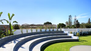 A modern outdoor area with a curved concrete structure, a well-maintained lawn, and a distant building with a unique architectural design.