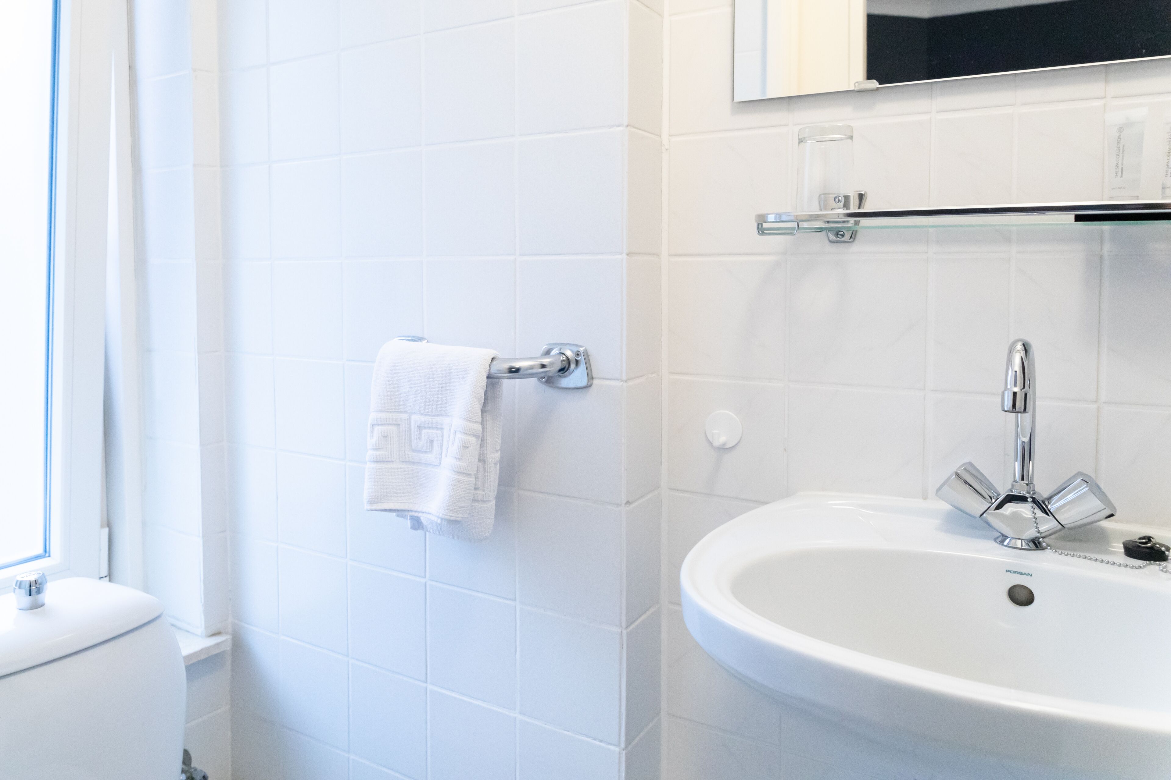 Ein Badezimmer mit einem weißen Waschbecken, einem Handtuch an einem Haken und einem Fenster.