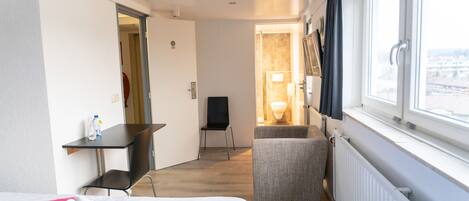 A hotel room with a bed, a desk, a chair, a small seating area, and a window with a view.