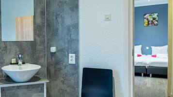 Een badkamer met een wit wastafel, een spiegel en een donkere stoel.