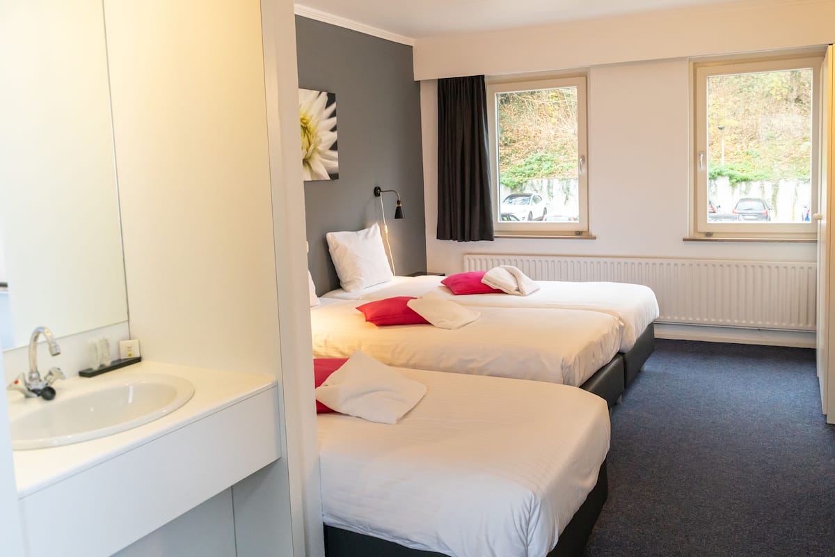 A hotel room with two beds, a white sink, and a window with a view of the outside.