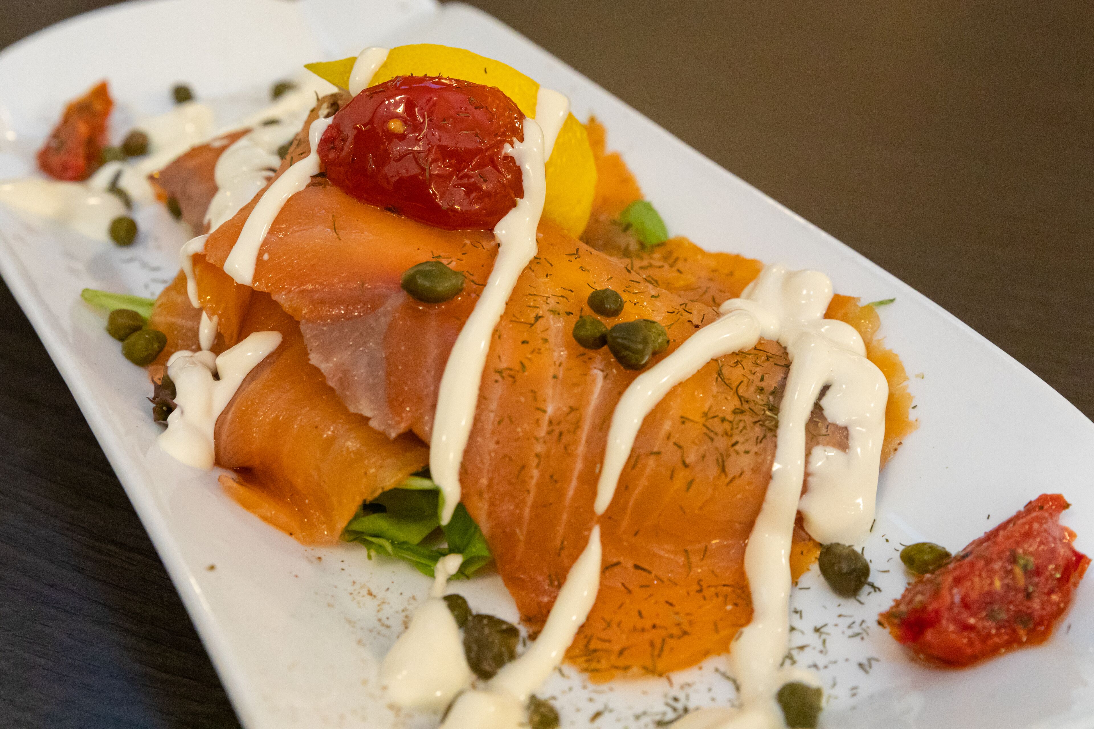 Een bord eten met zalm, kappertjes en een lepel saus.