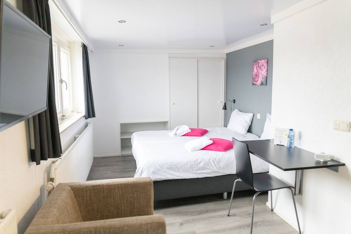 A hotel room with a bed, a desk, a chair, a TV, and a window with curtains.