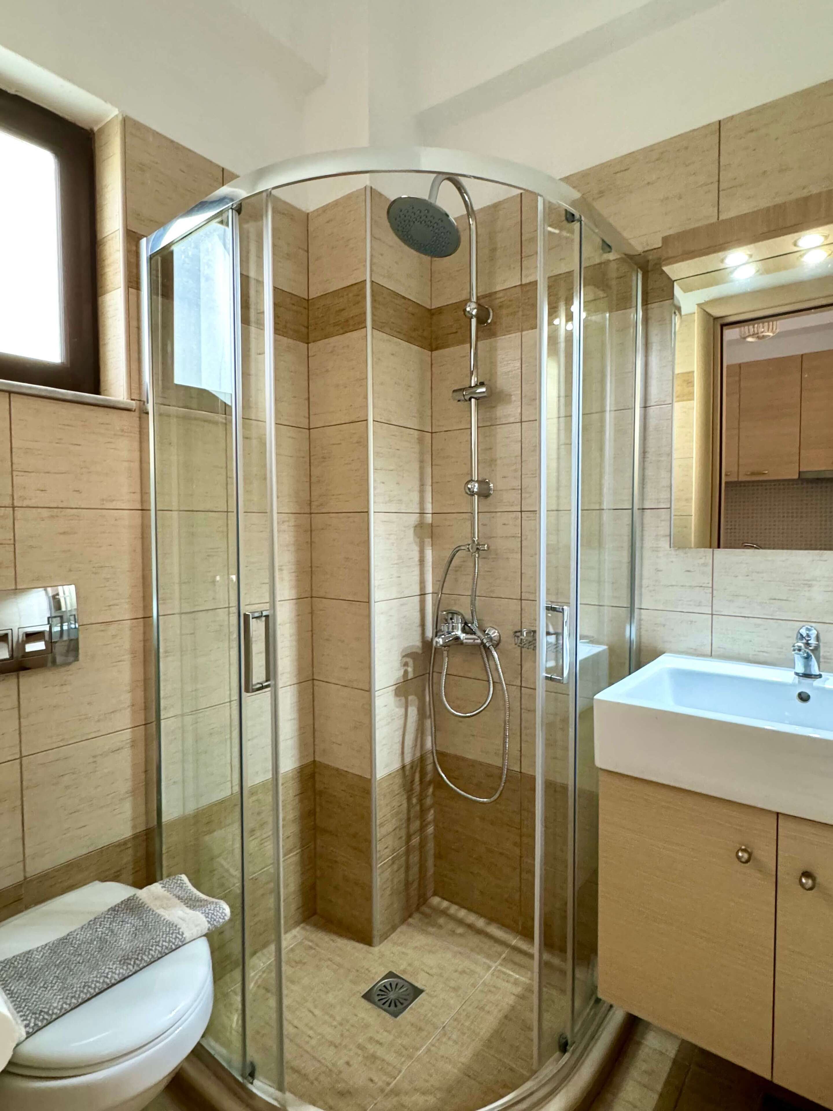 A modern bathroom with a glass-enclosed shower, a toilet with a towel, and a sink with a mirror.
